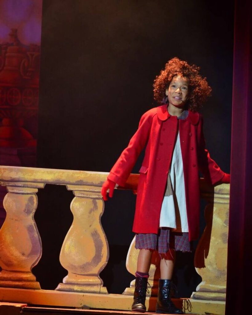 Annie in a red coat onstage 